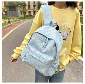 Detail of light blue backpack featuring embossed letter textures and colorful stitching