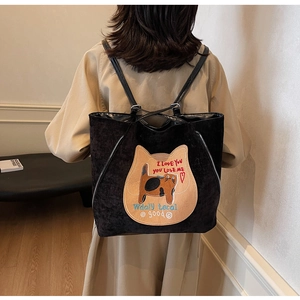 Rear view of a black corduroy tote with a cat patch embroidery on a model wearing an autumn coat