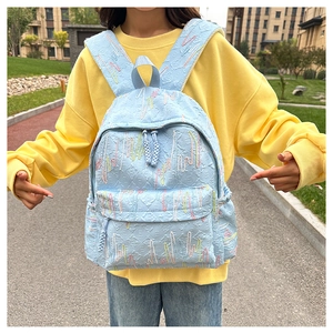 Detail of light blue quilted backpack with colorful wavy embroidery and zip pockets