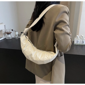 Side view of cream pleated croissant bag worn by model in a modern urban cafe setting