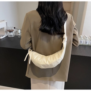 Detail of minimalist cream croissant bag with pleated stitching worn on the shoulder