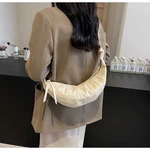 Close-up of beige quilted croissant bag worn as a crossbody on a stylish model