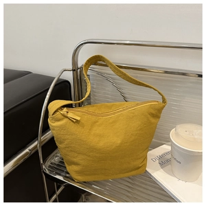 Detail of ginger yellow bucket bag with zipper closure and textured fabric on metal shelf