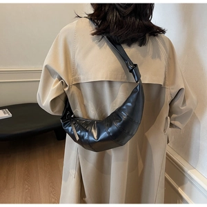 Detail of a black quilted croissant bag with a knotted shoulder strap and sleek zipper