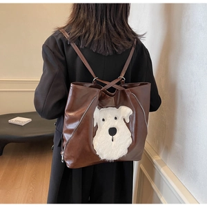 Detail of a large brown leather tote bag featuring a 3D plush white dog motif on the side