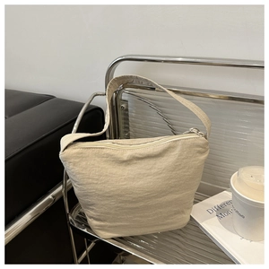 Detailed view of beige canvas bucket bag featuring zipper closure and wide shoulder strap