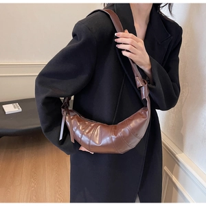 Detail of a deep brown shiny leather crescent bag with unique seam lines and knotted strap