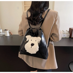Detail of black leather backpack featuring a cute white plush puppy patch and metal zipper