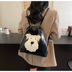 Detail of black glossy backpack with white plush cartoon dog patch worn by a model