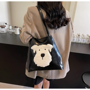 Detail of black faux leather tote featuring a white plush dog patch and long shoulder strap