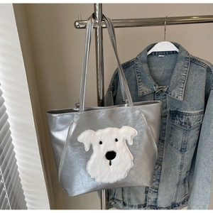 Detail of silver tote bag featuring a cute white plush dog patch and metallic finish