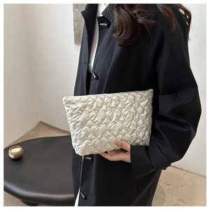 Detail of heart-quilted square bag in pearl white with metallic finish held by model