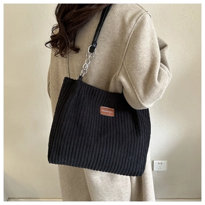 Close-up of black corduroy tote bag featuring silver chain straps and brand label