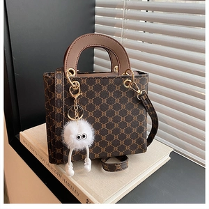 Detail of vintage tote bag with classic pattern, brown leather handles and plush charm