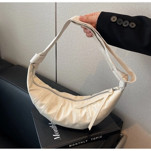 Detail of a creamy crescent crossbody bag with vertical quilting and decorative knots