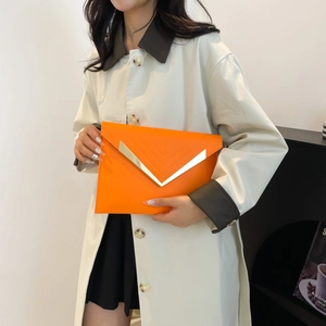 Chic orange envelope clutch bag with gold V-shaped buckle held by a model in a trench coat