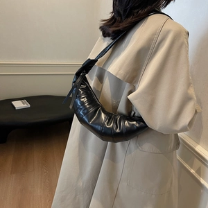 Minimalist black croissant shoulder bag with knotted details and glossy finish shown on model