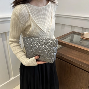 Silver heart quilted puffer clutch bag held by model showing stylish metallic texture