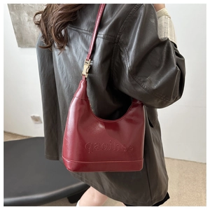 Close-up of burgundy leather underarm bag with gold buckle and embossed text on strap
