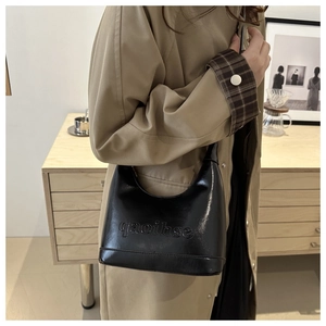 Detail of glossy black patent leather crescent bag with embossed qaoibse lettering