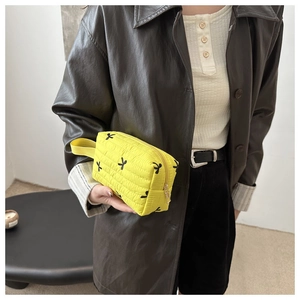 Close-up of yellow quilted clutch with black bow embroidery and side carrying strap
