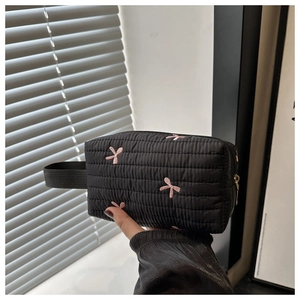 Detail of black quilted pouch with pink embroidered bows and gold zipper closure