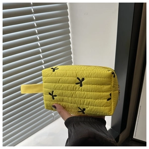 Detail of yellow quilted clutch bag with embroidered black bows and gold metal zipper