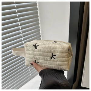 Detail of cream quilted nylon pouch with black butterfly embroidery and zipper
