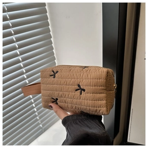 Close-up of khaki quilted hand pouch featuring black bow embroidery and zipper detail
