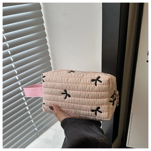 Detailed shot of pink quilted cosmetic bag featuring black bow embroidery and top handle