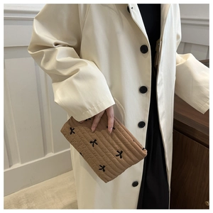 Detail of khaki quilted makeup bag with black bow embroidery held against a cream coat