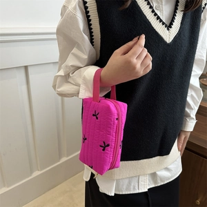 Magenta quilted cosmetic bag with black embroidery and handle in a casual setting