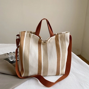 Détail du sac cabas en toile avec rayures, poignées marron et fermeture à bouton-pression
