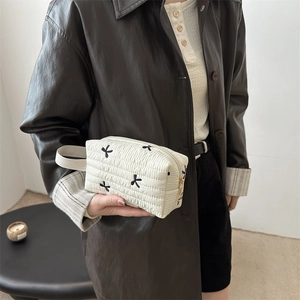 Quilted white cosmetic pouch with black bow embroidery and side handle for travel