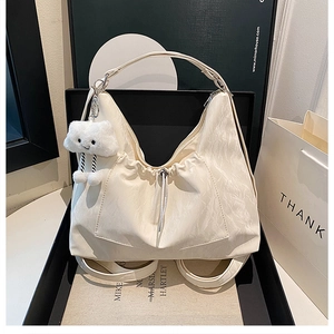 Detailaufnahme der beigen Hobo-Tasche mit Falten, Kordelzug und weißem Plüsch-Wolkenanhänger