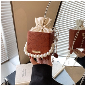 Detail der rotbraunen Eimer-Tasche mit Blumenprägung, Perlengriff und Goldkette