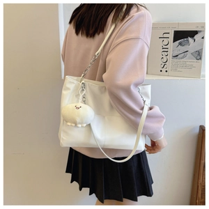 Detail of white tote bag with silver chain strap and plush pendant on model