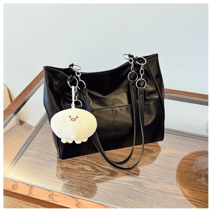 Detail of black faux leather tote bag with silver ring hardware and cute plush charm