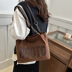 Brown suede tote bag with HOOTO lettering and gold chain strap worn by a model