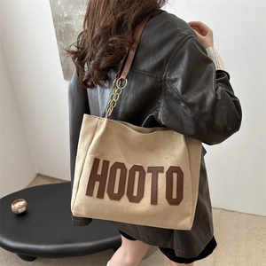 Chic beige tote bag with HOOTO leather letters and chain strap shown on a model