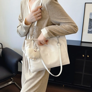 Minimalist white tote bag with metal chain straps and plush charm shown from a side view