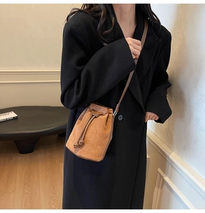 Brown suede bucket bag with leather drawstring detail styled on a black wool coat
