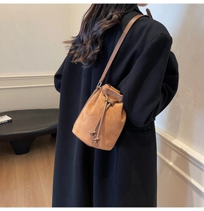 Brown faux suede bucket bag with drawstring closure worn by model in black coat