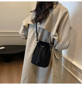 Dettaglio della borsa a secchiello in nylon nero con coulisse indossata con un trench beige