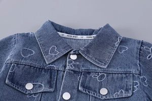 Detail of washed blue denim jacket with white heart embroidery and round buttons
