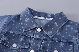 Détail d'une veste en jean bleue pour filles avec imprimés nœuds blancs et cœurs