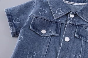 Detail of blue denim shirt for toddlers featuring white heart embroidery and metal snaps