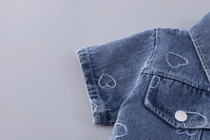 Detail of blue denim jacket showing heart pattern and flap pocket with metal button