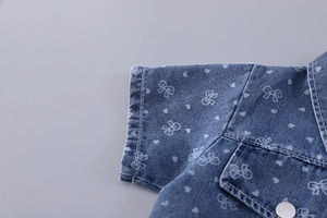 Détail d'un haut en jean bleu avec imprimés cœurs et nœuds blancs et boutons métalliques