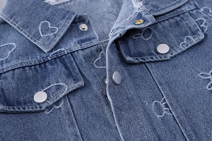 Detailed view of denim jacket featuring heart-shaped white stitching and metal snap buttons